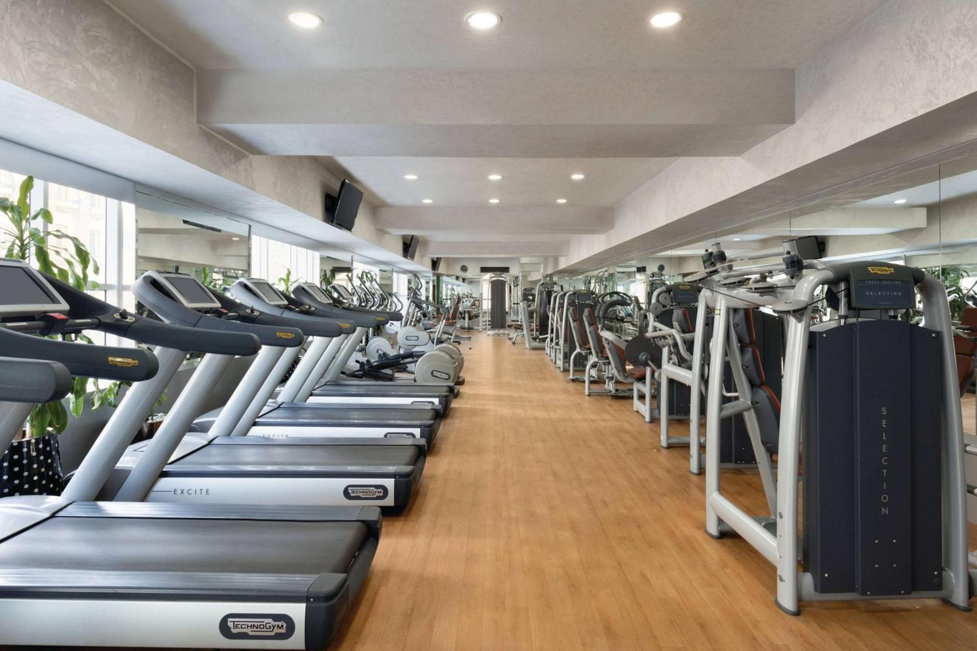فندق ويندهام جراند ريجنسي الدوحة المظهر الخارجي الصورة The photo shows the interior of a gym or fitness center. It features a row of modern treadmills lined up against a wall, with a polished wooden floor. The space is brightly lit with recessed ceiling lights, and there are large mirrors on the walls, e